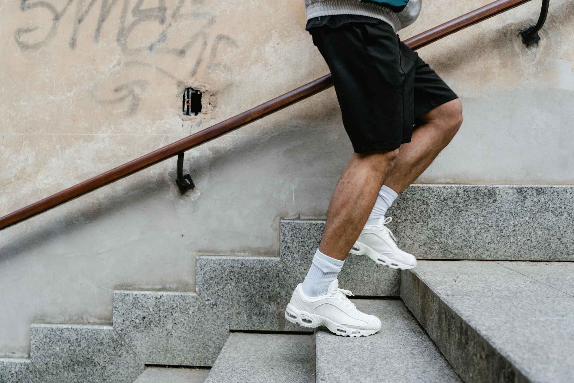 Close-up of a person''s legs climbing outdoor stone steps in running shoes — illustrating the impact loading that irritates the Achilles, knees, and shins when reintroduced too quickly