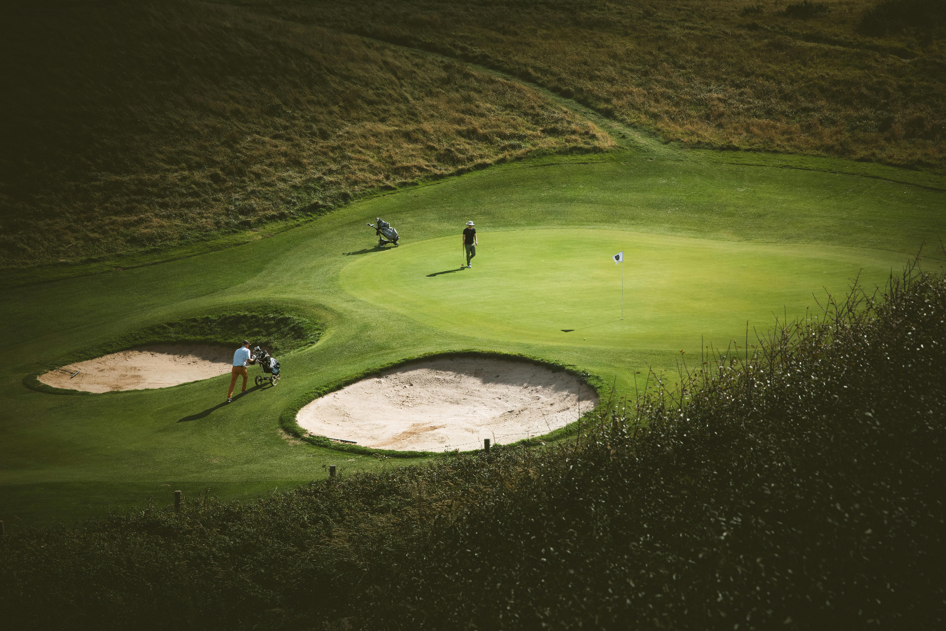Two golfers on a manicured green with bunkers and rolling dune-side rough, representative of the Costa del Sol courses our patients play throughout the season