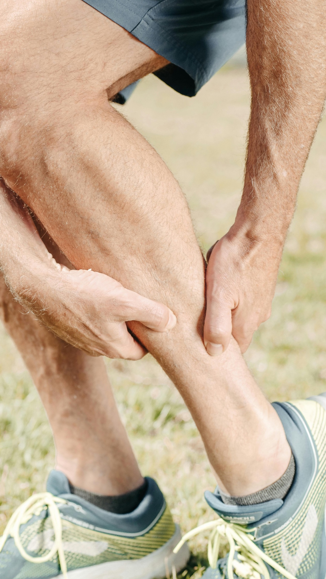 Runner outdoors gripping his calf muscle in pain after a training session — a classic acute sports injury treated with early physiotherapy on the Costa del Sol