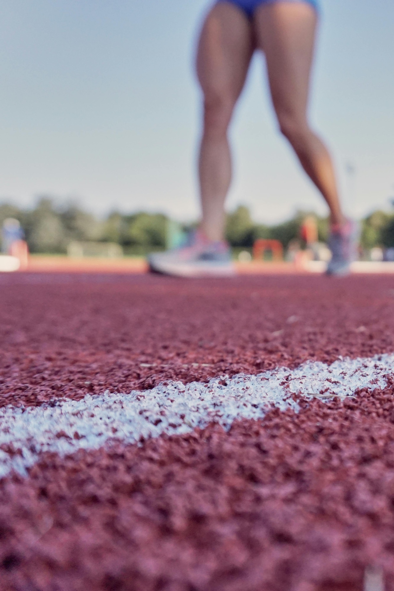 Female runner training on an outdoor athletics track, viewed from ground level — illustrating gradual load progression and structured return-to-running programmes